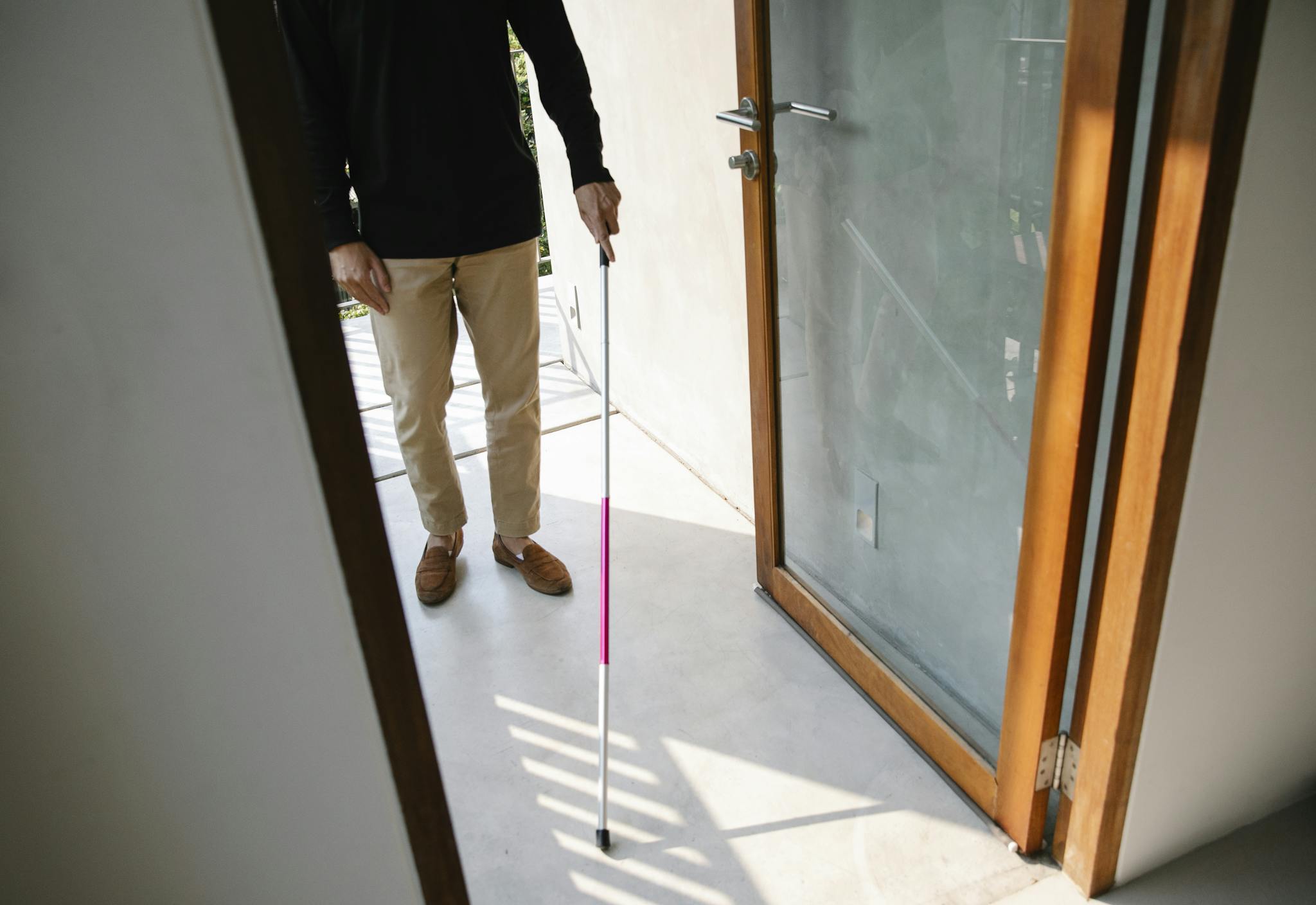 Person with visual impairment using a cane to enter a house, symbolizing independence.